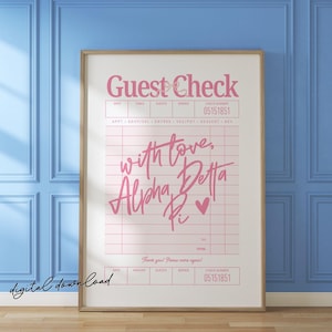 May include: A framed print featuring a pink "Guest Check" design with handwritten text that reads "with love, Alpha Pi" and a heart symbol. The print is in a wooden frame and is set against a blue wall.
