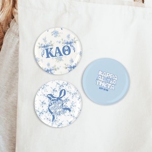 May include: Three round buttons with floral and text designs. One button has "KAO" in blue on a floral background. Another has "Kappa Alpha Theta" with a bow graphic. The third button is light blue with "Kappa Alpha Theta EST 1870".