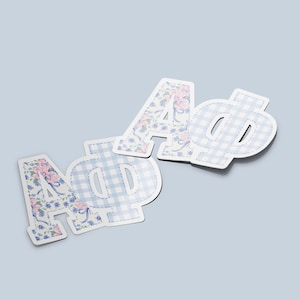 May include: Decorative Greek letters, including Alpha and Phi, in a floral and gingham pattern. The letters are white with a light blue and pink floral design, and a light blue and white gingham pattern.