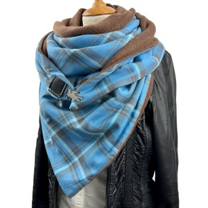 Könnte beinhalten: Ein blauer und brauner karierter Schal mit Fleecefutter. Der Schal hat einen Metallverschluss und wird über einer schwarzen Lederjacke getragen.