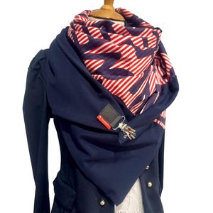 Könnte beinhalten: Eine marineblaue Jacke mit einem rot-weiß gestreiften Schal mit einem blauen Muster. Der Schal ist um den Hals gebunden und hängt an der Vorderseite der Jacke herunter.