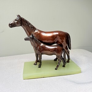 Escultura antigua de metal de yegua y potro montada sobre una base de ónix verde.