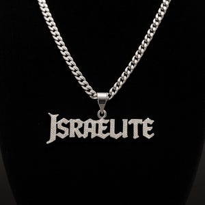 May include: A silver-colored necklace with a chain and a pendant that spells out "ISRAELITE" in a gothic font. The pendant is encrusted with small, sparkling stones. The background is black.