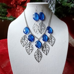 This necklace is designed with shiny silver filigree leaves and royal blue acrylic beads on a silver-plated metal chain.