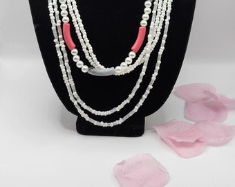 Adalah est un magnifique ensemble de colliers multirangs gris, rose et blanc audacieux. Les boucles d'oreilles sont des tubes blancs avec des strass roses et une fausse perle.