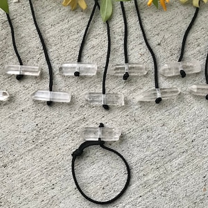 May include: A set of clear quartz crystal points strung on black cords. The crystals are various sizes and shapes. The cords are tied together at the top, creating a hanging display.