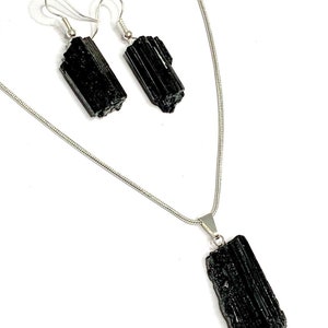 Puede incluir: Un conjunto de collar y pendientes de turmalina negra con cadena y ganchos de plata. El collar presenta un gran colgante de turmalina negra en bruto.