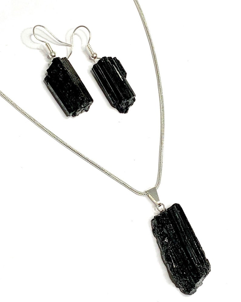 Puede incluir: Un conjunto de collar y pendientes de turmalina negra con cadena y ganchos de plata. El collar presenta un gran colgante de turmalina negra en bruto.