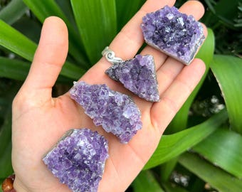 May include: Four raw amethyst crystal clusters with deep purple, jagged, crystalline surfaces. One cluster is set in a silver-toned metal pendant with a bail, while the other three are loose, irregular, angular pieces of natural purple quartz stone.