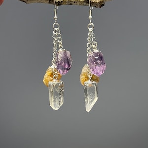 Puede incluir: Un par de pendientes de plata con un cristal de cuarzo transparente, amatista y citrino. Los pendientes están hechos con una cadena de plata y tienen un diseño sencillo.
