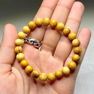 A bracelet made of light brown wooden beads. The beads are round and have a smooth, polished finish. The bracelet is strung on a thin, clear cord.