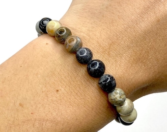 May include: A bracelet made of round, multi-colored stones. The stones are arranged in a gradient pattern, starting with light brown and transitioning to dark gray.