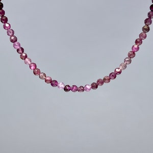 Puede incluir: Un delicado collar hecho de pequeñas piedras preciosas facetadas de color rosa y morado. El collar está hecho de una sola hebra de cuentas y tiene un diseño simple y elegante.