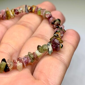 A bracelet made of small, irregular shaped, multi-colored gemstones. The gemstones are shades of pink, green, brown, and black.