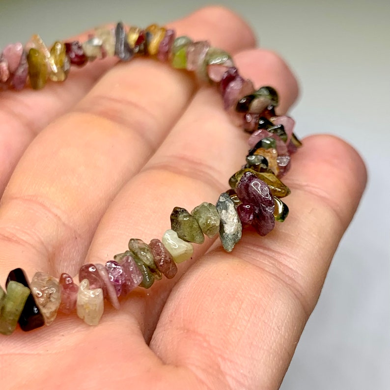 A bracelet made of small, irregular shaped, multi-colored gemstones. The gemstones are shades of pink, green, brown, and black.