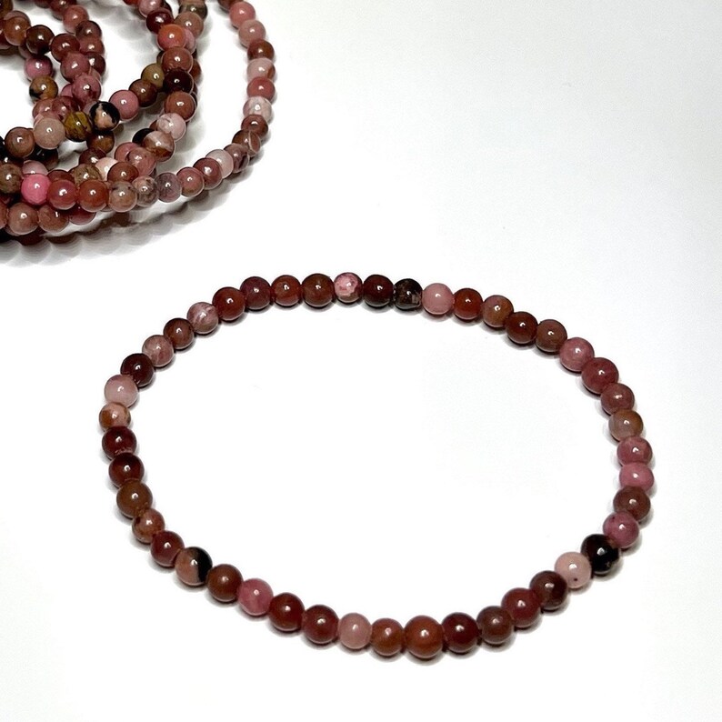 A pink and brown beaded bracelet made of natural stones. The bracelet is made of small, round beads that are strung together on a thin cord. The beads are a mix of pink and brown colors, and they have a natural, polished finish.