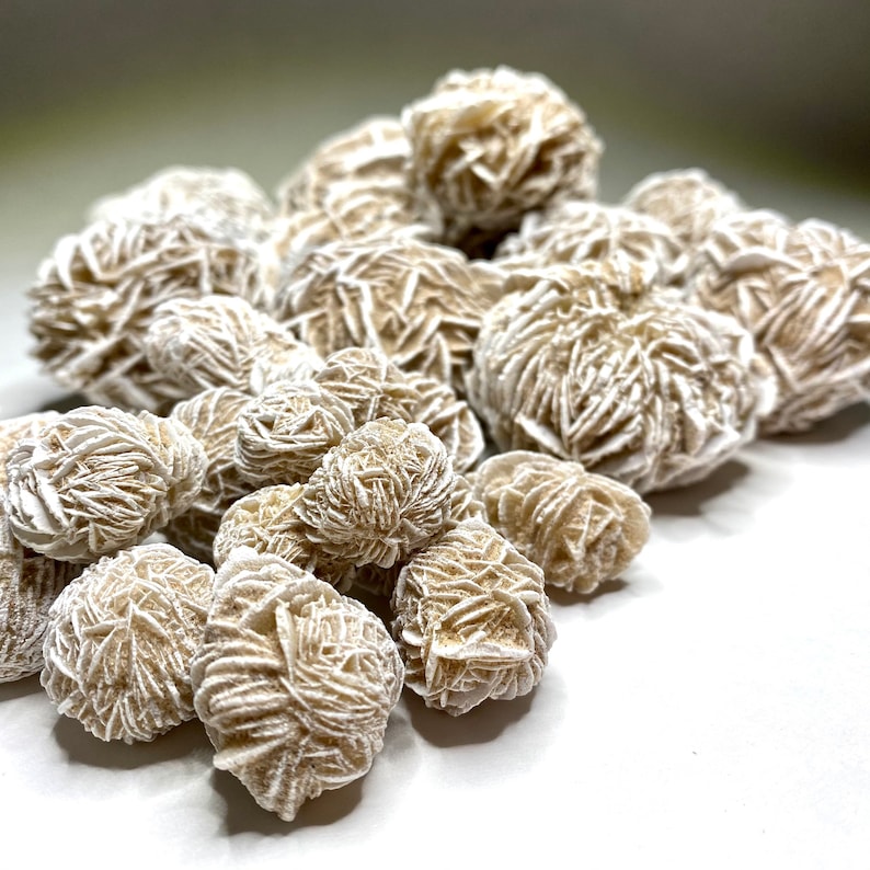 A group of white and tan desert rose crystals. The crystals are clustered together and have a rough, textured surface.