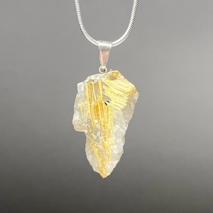 May include: A silver chain necklace with a clear quartz pendant containing gold rutile inclusions. The pendant is a rough, irregular shape.