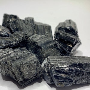 A collection of black tourmaline crystals, also known as schorl, with a rough, natural texture. The crystals are various sizes and shapes, with some showing striations.