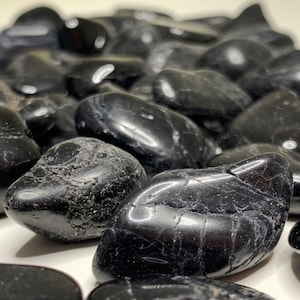 Op de afbeelding: Een verzameling gladde, zwarte obsidiaan-tumbled stenen. De stenen zijn van verschillende groottes en vormen, met een glanzende afwerking.