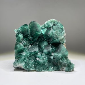 May include: A cluster of green fluorite crystals with a rough, natural texture. The crystals are intergrown and have a variety of shapes and sizes.