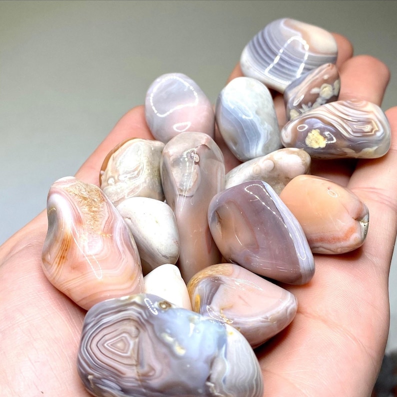 A collection of smooth, polished agate stones in various shades of pink, white, and gray. The stones have intricate banding patterns and a glossy finish.