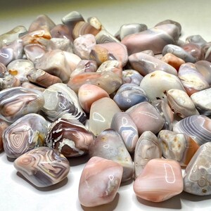 A collection of pink, white, and gray agate tumbled stones. The stones are smooth and have a variety of patterns and textures.
