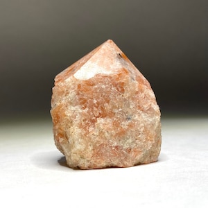 Pode incluir: Um cristal áspero de cor laranja-marrom com uma ponta pontiaguda. O cristal tem um aspecto natural e não polido.