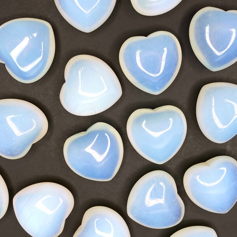 A collection of heart shaped blue and white opalite stones on a black surface.