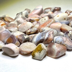 A collection of tumbled agate stones in various shades of pink, brown, and white with intricate banding patterns.