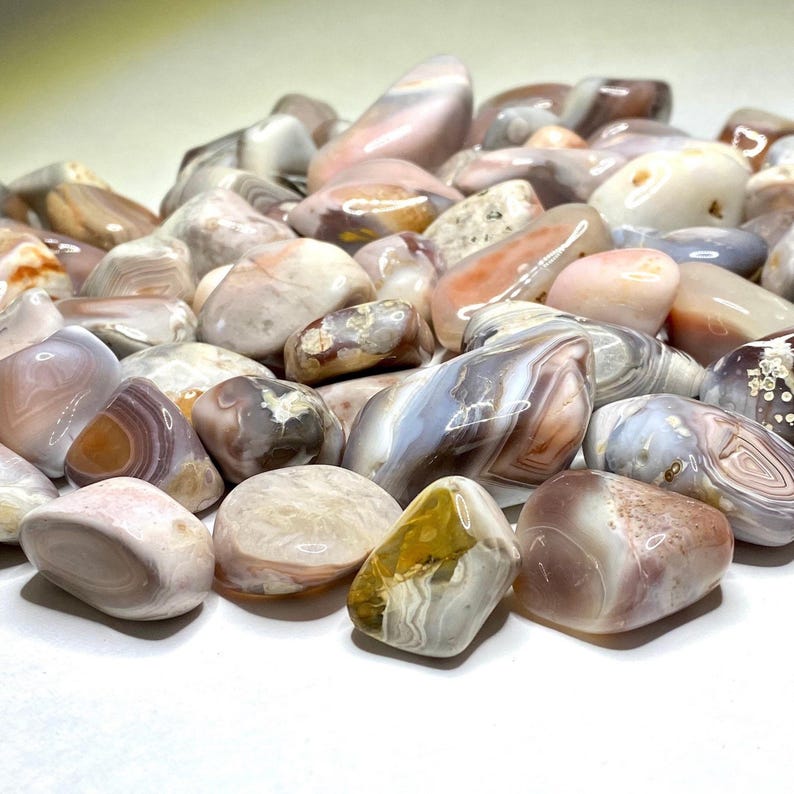 A collection of tumbled agate stones in various shades of pink, brown, and white with intricate banding patterns.