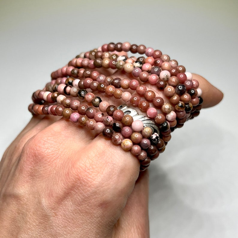 A stack of pink, brown, and white gemstone beads. The beads are round and have a smooth, polished finish. The beads are strung together on a clear elastic cord.