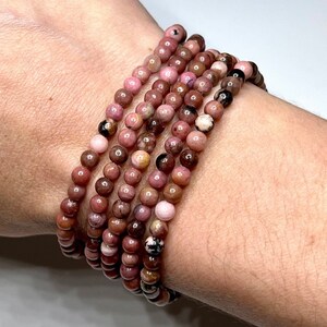 A stack of pink and brown beaded bracelets made of natural stone. The bracelets are made of round beads and are stacked on top of each other.