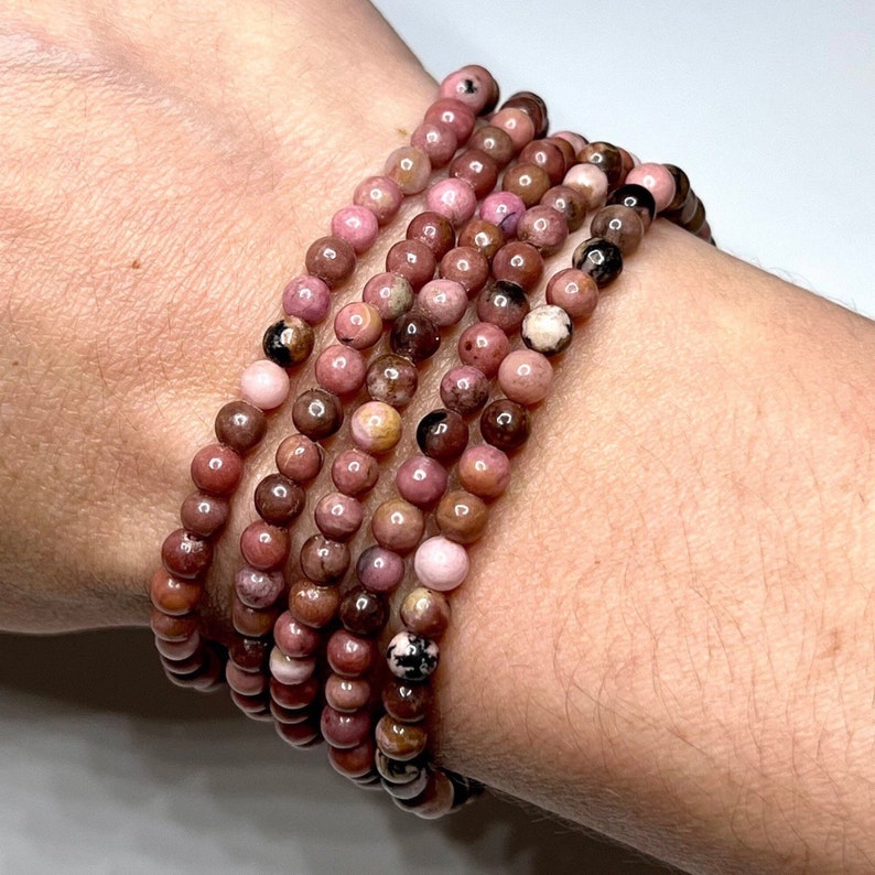 A stack of pink and brown beaded bracelets made of natural stone. The bracelets are made of round beads and are stacked on top of each other.