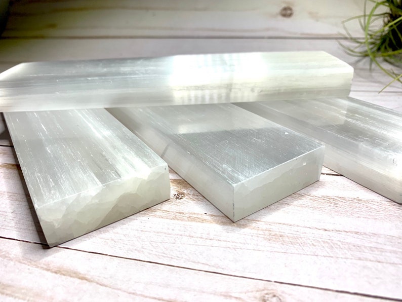 Four selenite crystal bars stacked on top of each other. The bars are white and have a smooth, polished surface. The bars are arranged in a staggered pattern.