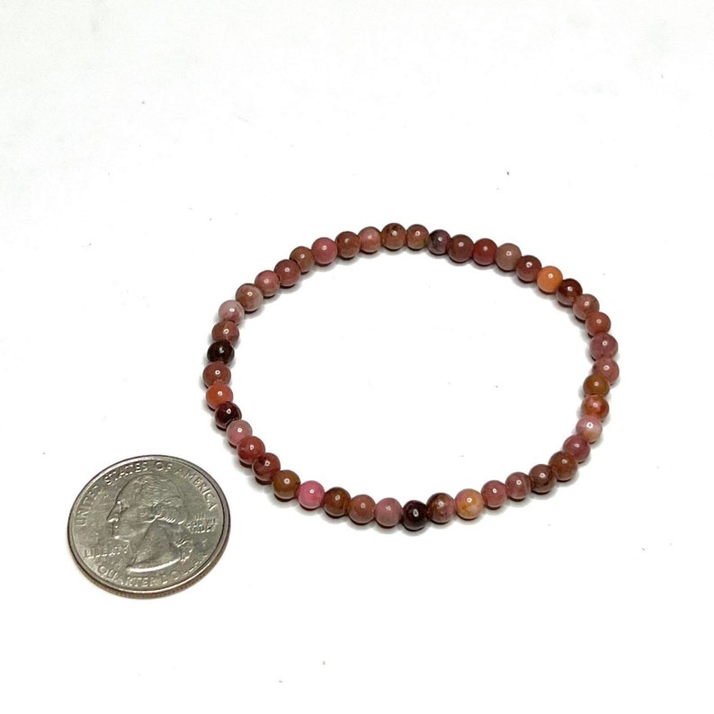 A pink and brown beaded bracelet with a silver clasp. The bracelet is made of small, round beads and is about the size of a quarter.