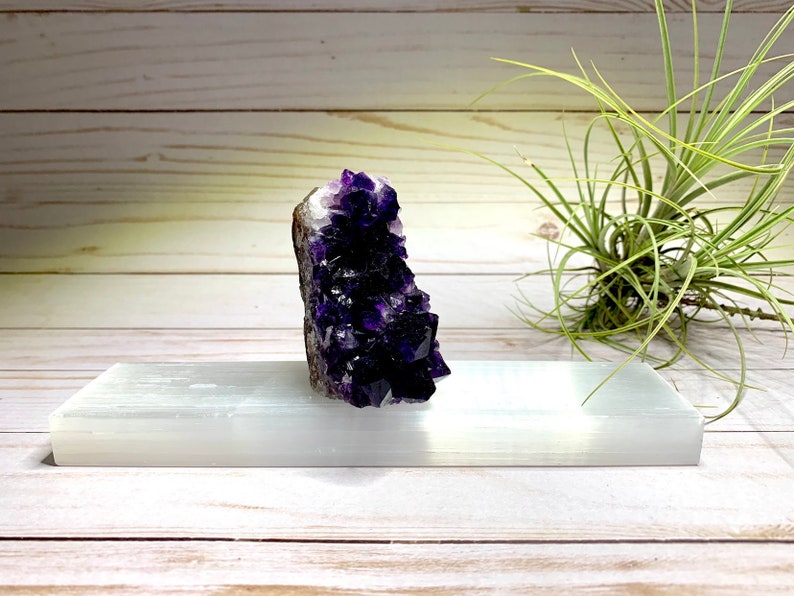 A large amethyst crystal cluster with a deep purple color. The crystal is sitting on a white selenite charging plate.