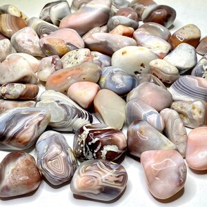 A collection of pink, white, and gray agate tumbled stones from Botswana. The stones have a variety of patterns and textures. The stones are smooth and polished.
