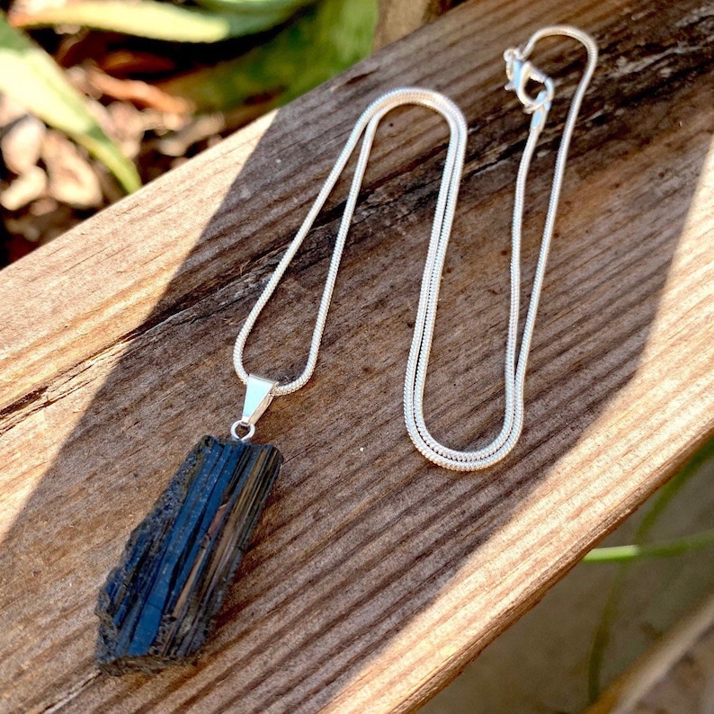 Puede incluir: Un collar de cadena de plata con un colgante de turmalina negra. El colgante es una pieza bruta de turmalina negra sin pulir.