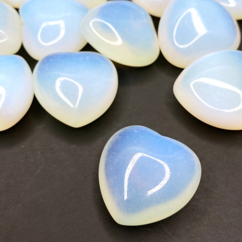 A group of heart shaped polished opalite stones. The stones are a milky white color with a slight iridescent sheen.