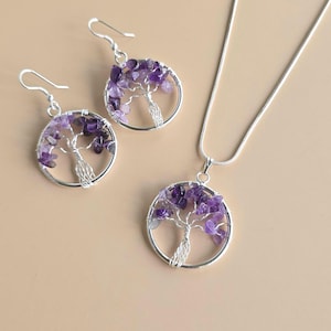Può includere: Un set di gioielli color argento con collana con pendente e orecchini abbinati. Ogni pezzo presenta un design ad albero con una cornice circolare, adornato con pietre di ametista viola. Gli orecchini hanno chiusure a gancio.