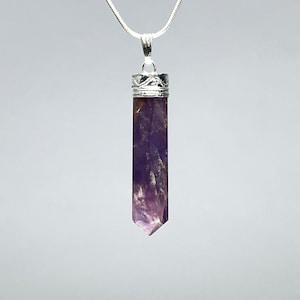 May include: A silver chain necklace with a purple amethyst crystal pendant. The pendant is faceted and has a silver cap at the top.