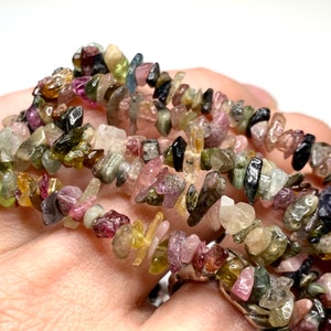 A strand of multi-colored chip gemstone beads. The beads are a mix of pink, green, black, and yellow. The beads are irregular in shape and have a rough, natural texture.