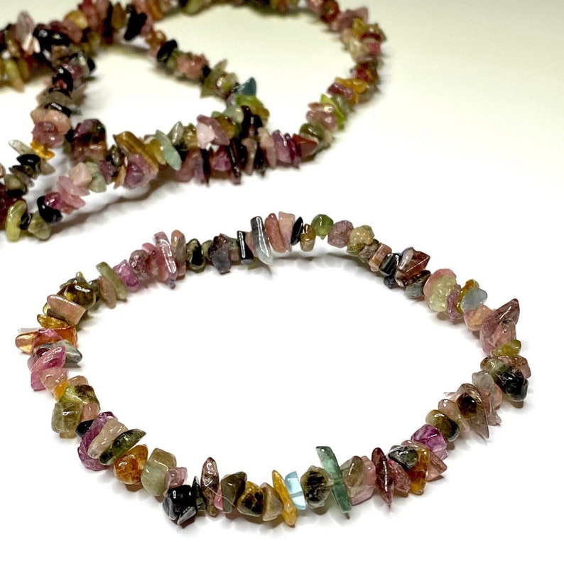 A bracelet made of small, chipped, multi-colored gemstones. The bracelet is made of pink, green, brown, black, and blue gemstones. The bracelet is on a white background.