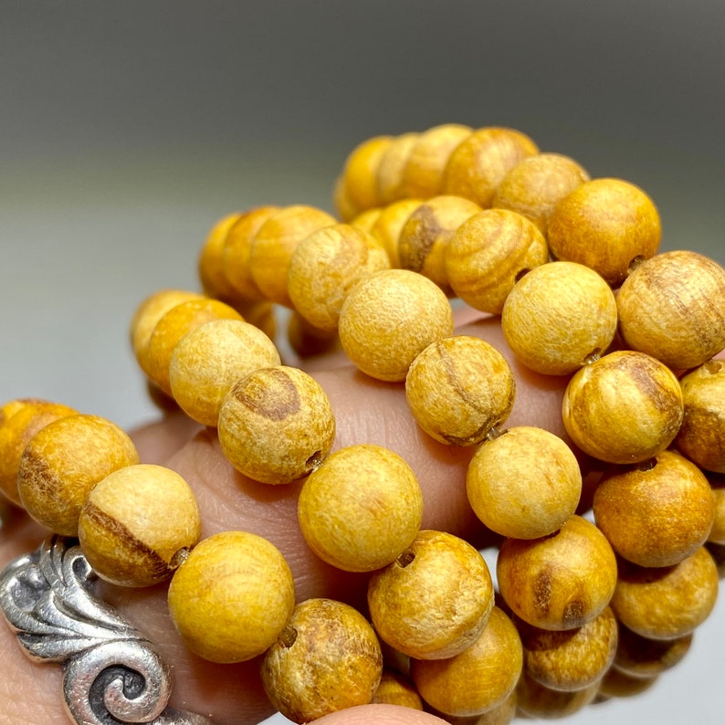 A string of round, wooden beads. The beads are a light yellow color with brown streaks. The beads are arranged in a circular pattern.