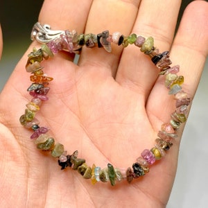 A bracelet made of small, irregular shaped gemstones in various colors including pink, green, brown, black, and clear. The bracelet is made of natural, unpolished gemstones.
