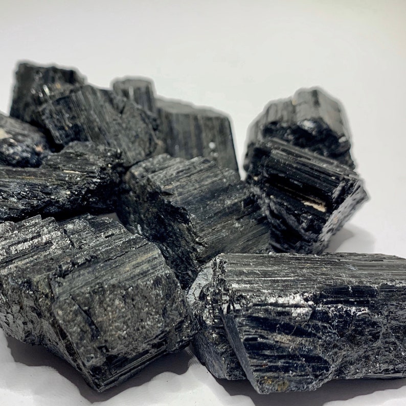 A collection of black tourmaline crystals, also known as schorl, with a rough, natural texture. The crystals are various sizes and shapes, with some showing striations.