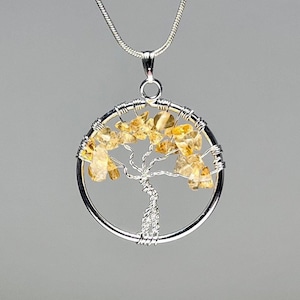 May include: A silver wire wrapped tree of life pendant with a circular design. The tree is adorned with small, light yellow citrine stones.