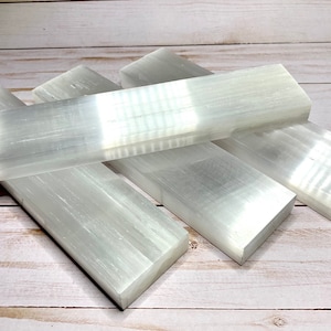 Four selenite crystal wands stacked on top of each other. The bars are white and have a smooth, polished surface. The bar are rectangular in shape and have a slight taper at one end.