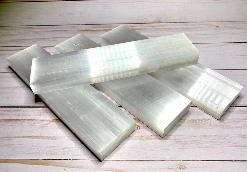 Four selenite crystal wands stacked on top of each other. The bars are white and have a smooth, polished surface. The bar are rectangular in shape and have a slight taper at one end.